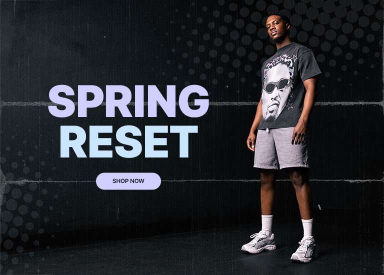 A wide horizontal banner titled SPRING RESET in large light blue and purple text. It features two images of a man in a dark grey graphic t-shirt with a portrait on it, grey fleece shorts, white socks, and white Asics 2160 sneakers. The background is dark with a subtle grey polka-dot pattern.