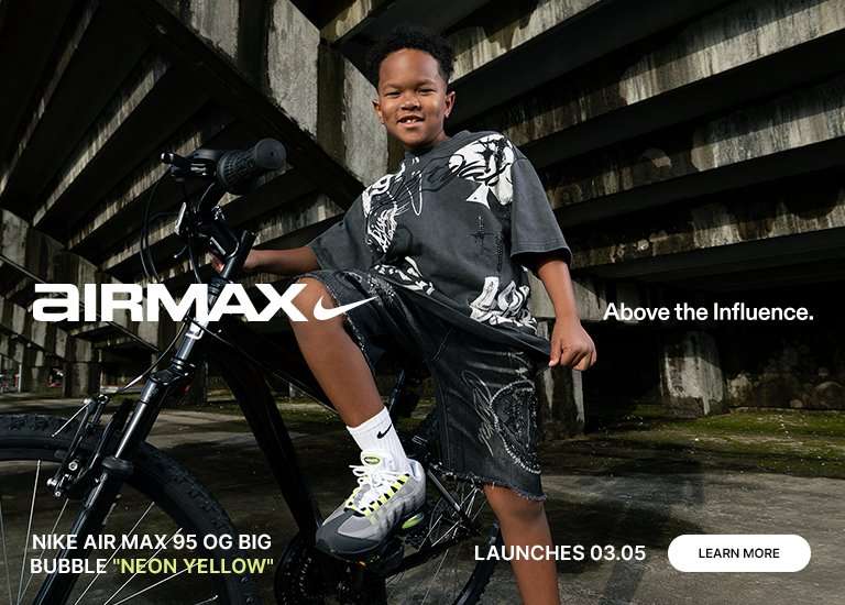 Promotional banner for the Nike Air Max 95 OG Big Bubble Neon Yellow featuring a young boy sitting on a black bicycle under a concrete overpass. He wears a graphic t-shirt, denim shorts, and the grey and neon yellow sneakers. To the right, a large close-up highlights the shoes and white Nike socks. The image includes the Air Max logo, the slogan Above the Influence, and a launch date of 03.05.