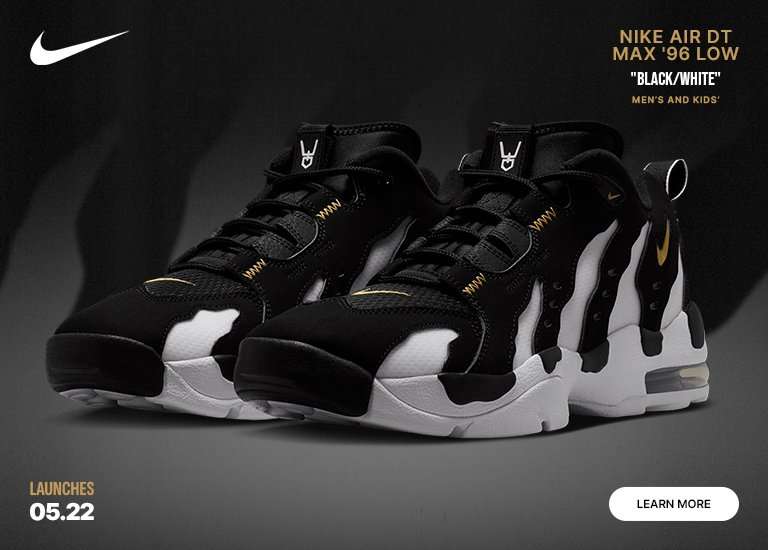 A digital marketing banner features a pair of Nike Air DT Max 96 Low Black/White sneakers against a dark, smoky background. The athletic shoes showcase a bold, flame-like black and white torn-paper design with gold accents. A white Nike swoosh sits in the top-left corner, while text in the top-right displays the shoe model for men and kids. The bottom corners include the launch date 05.22 and a white learn more button.