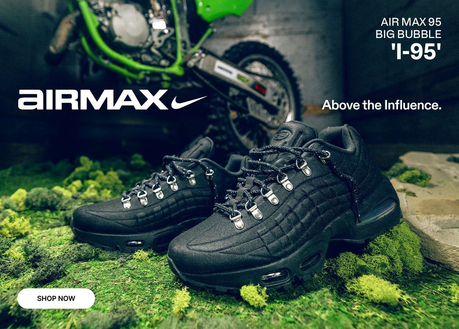 An advertisement for Nike Air Max 95 Big Bubble 'I-95' sneakers. The black, rugged, boot-like shoes with metal eyelets are displayed on a bed of green moss. In the background, a green dirt bike is partially visible. Text reads AIRMAX, Above the Influence, and a SHOP NOW button is in the bottom left corner.