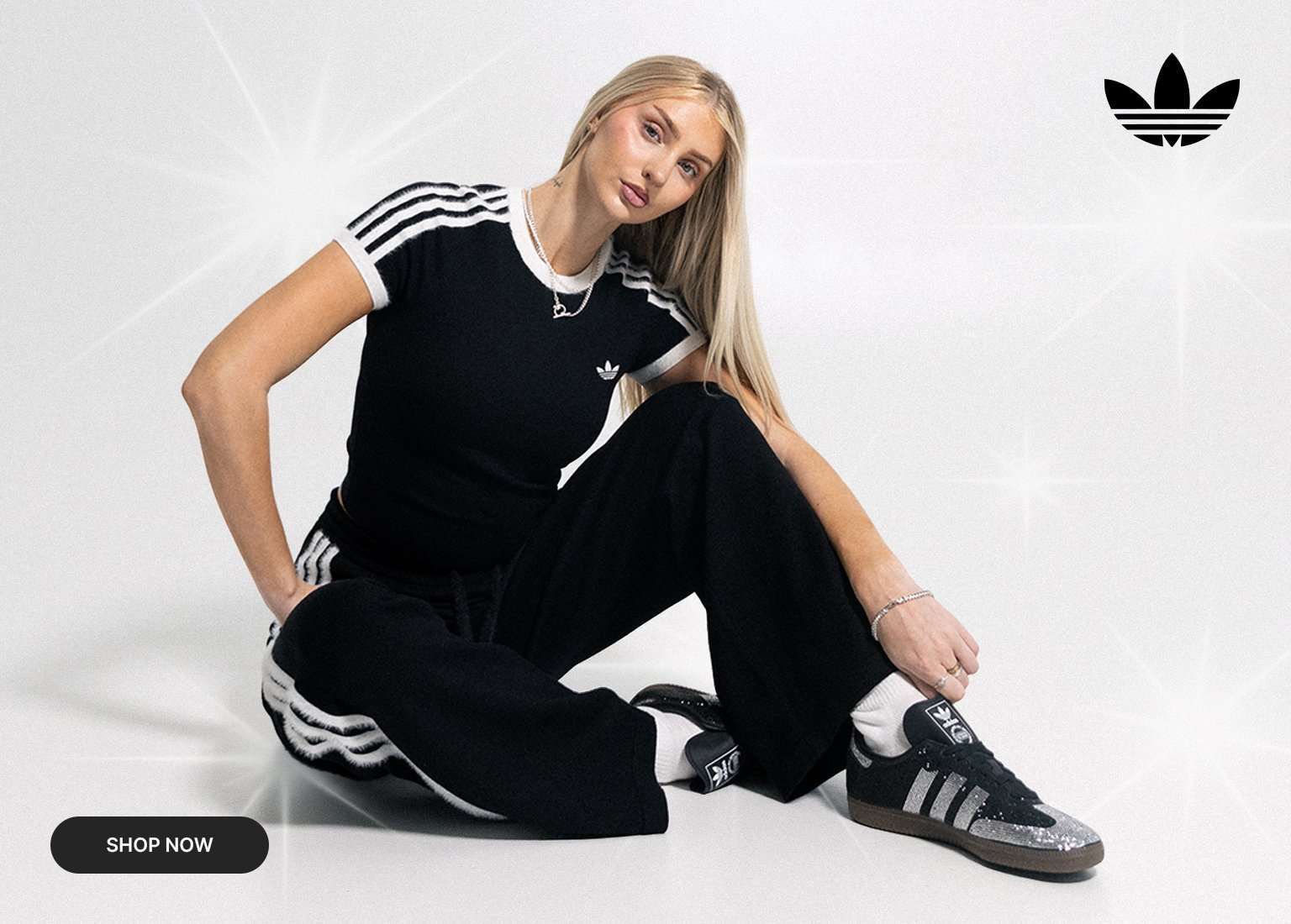 Model wearing a black Adidas three-stripe outfit and sneakers in a studio fashion campaign.