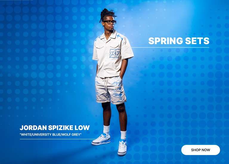 A male model wearing a cream-colored patterned short-sleeve shirt and matching shorts, paired with Jordan Spizike Low sneakers in White/University Blue/Wolf Grey.