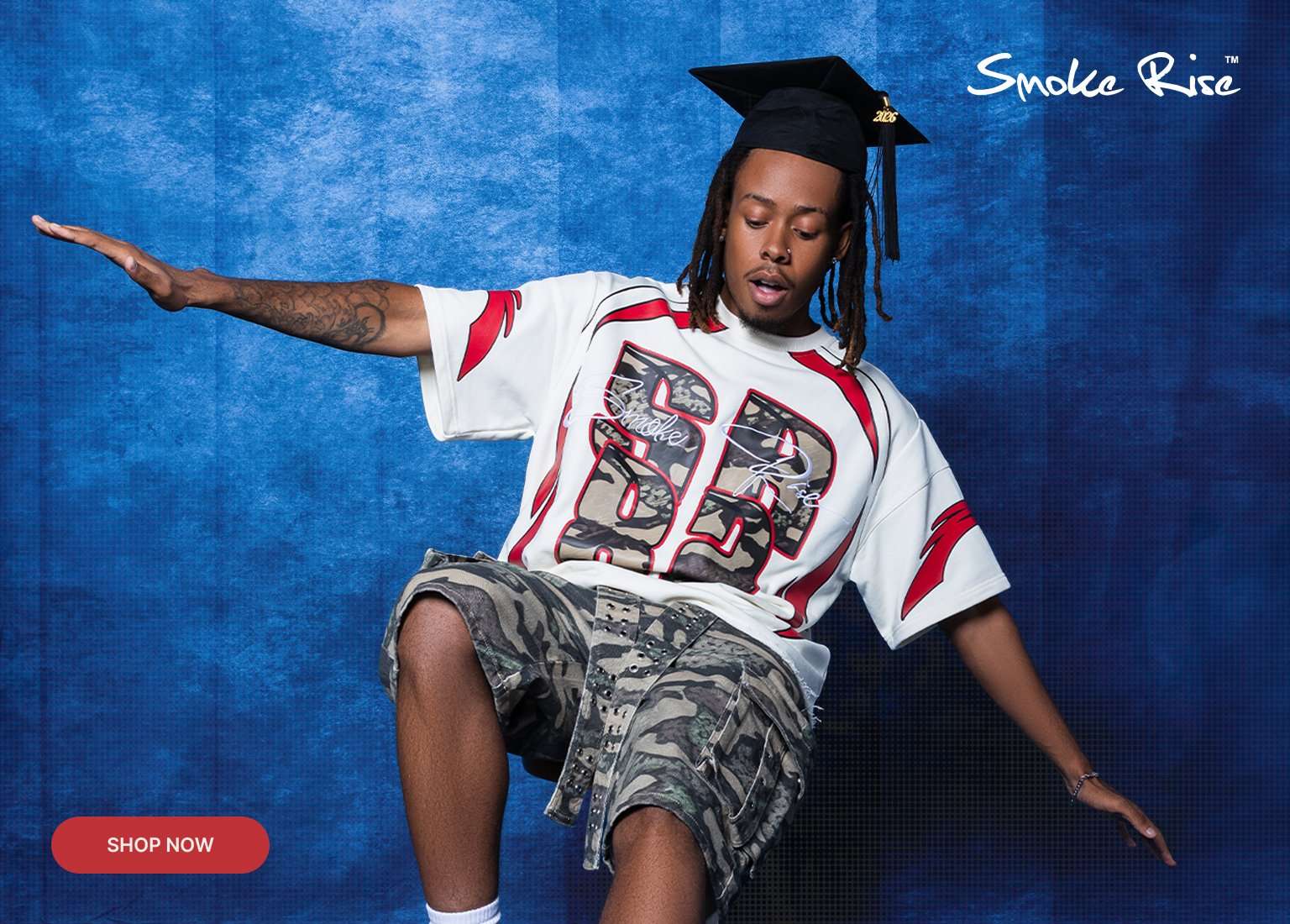 Banner for Smoke Rise featuring a man in a graduation cap wearing a white streetwear t-shirt with red accents and camo-patterned 82 graphics. He is shown from the front balancing on one leg and from the back showcasing the text Seize the moment. The background is a textured blue with a red Shop Now button.