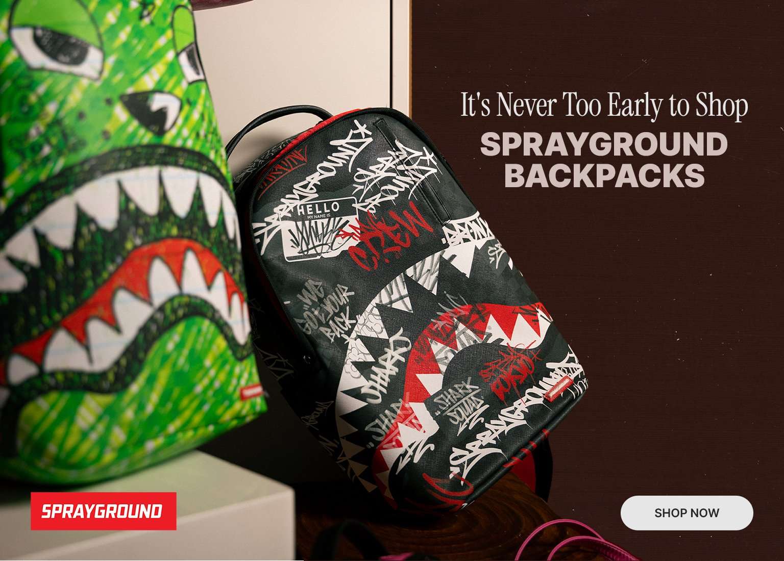 Promotional image featuring two colorful Sprayground backpacks with signature shark mouth designs. Text reads: It's Never Too Early to Shop SPRAYGROUND BACKPACKS, alongside a SHOP NOW button.