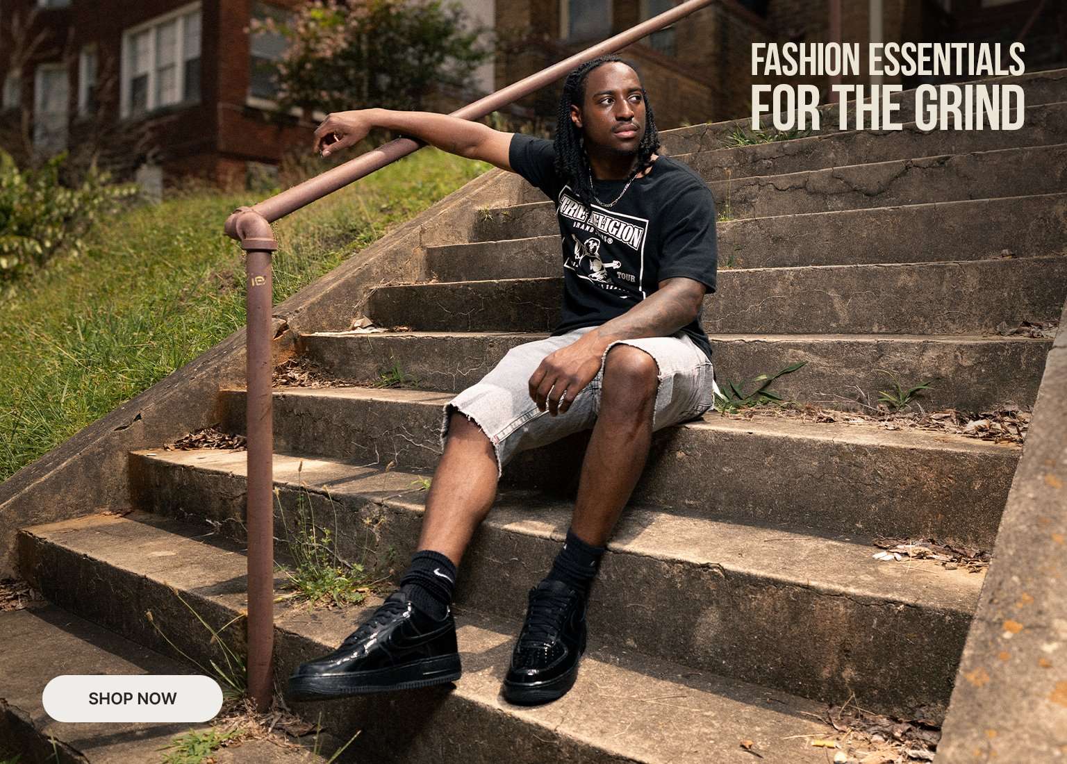 A multi-panel marketing banner featuring a man modeling True Religion apparel in an urban setting. The left panel shows a close-up of him wearing a black graphic t-shirt with a Shop Now button. The center panel shows him sitting on outdoor concrete steps. The right panel shows him standing next to a car with text reading Fashion Essentials For The Grind.