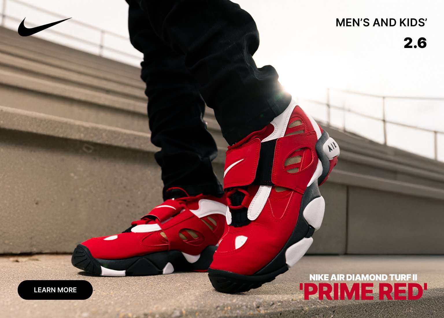 Red, white, and black Nike Air Diamond Turf II Prime Red sneakers on feet, shown outdoors on concrete steps with Nike logo and Men’s and Kids text.