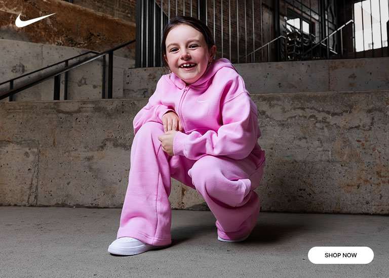 Kids' Nike pink fleece hoodie and wide-leg sweatpants with white Nike sneakers, shop now promotion.