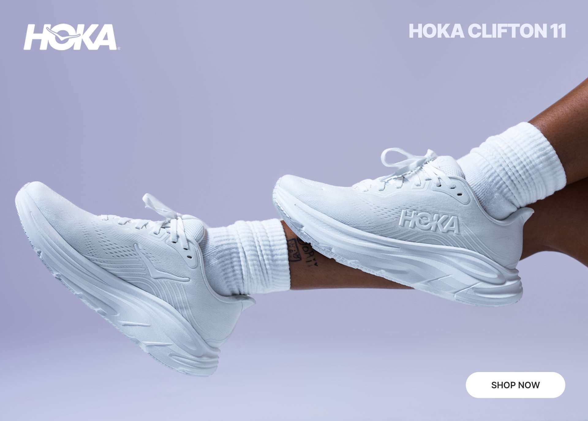 HOKA Clifton 11 all-white running shoe on foot against a light purple background with HOKA logo.