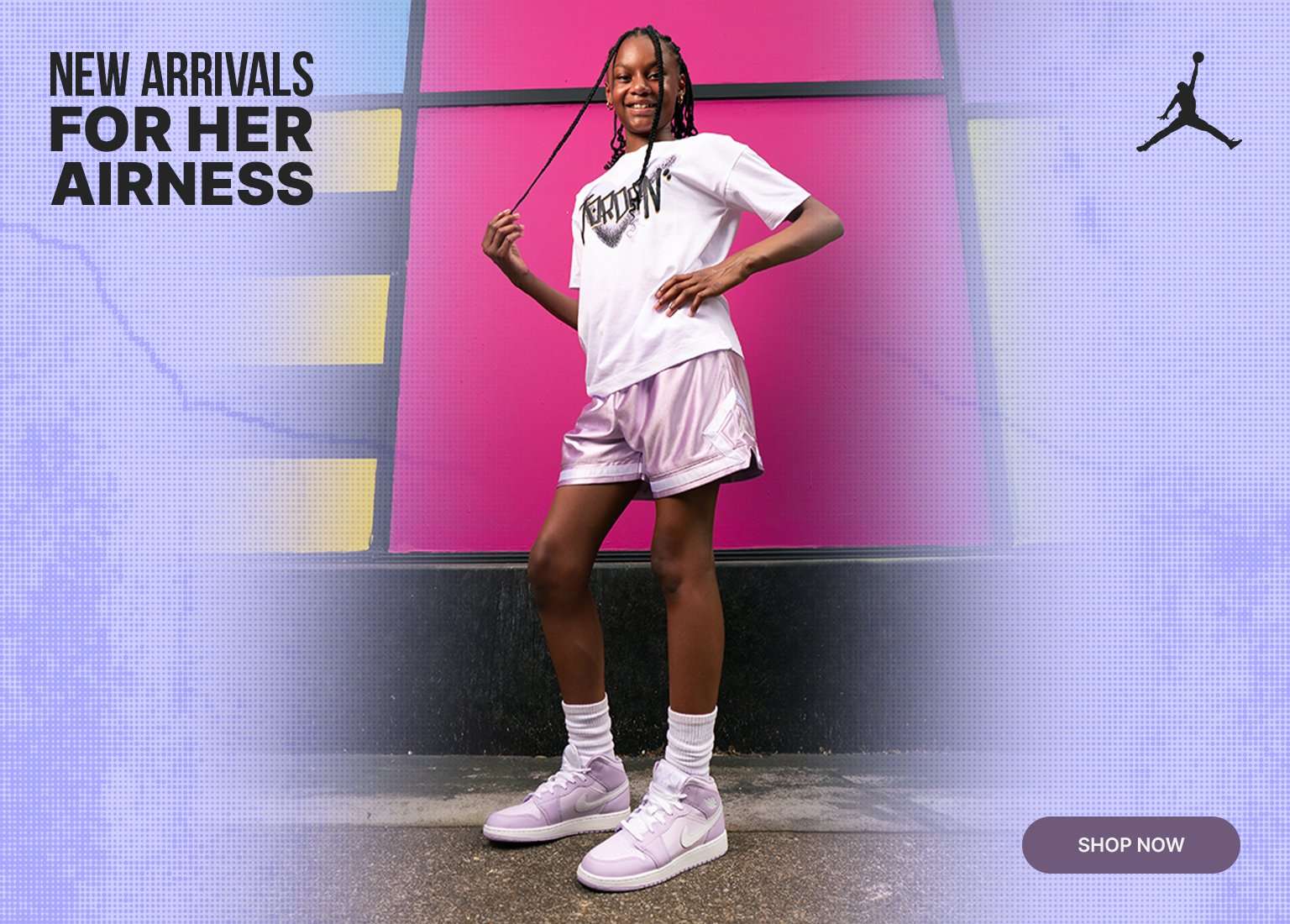 A promotional retail banner featuring a young girl posing in a white Jordan graphic t-shirt, shiny lavender athletic shorts, and purple and white Air Jordan 1 mid sneakers. She stands against a vibrant, color-blocked wall of pink, yellow, and green. The banner includes a textured lavender border, a black Jordan Jumpman logo, a Shop Now button, and the text New Arrivals For Her Airness.