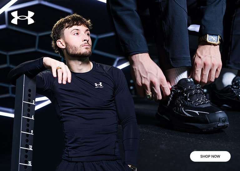 Under Armour performance apparel and black training shoes in a gym setting, featuring a model in a fitted black top beside a close-up of laced athletic footwear with neon geometric lighting in the background.