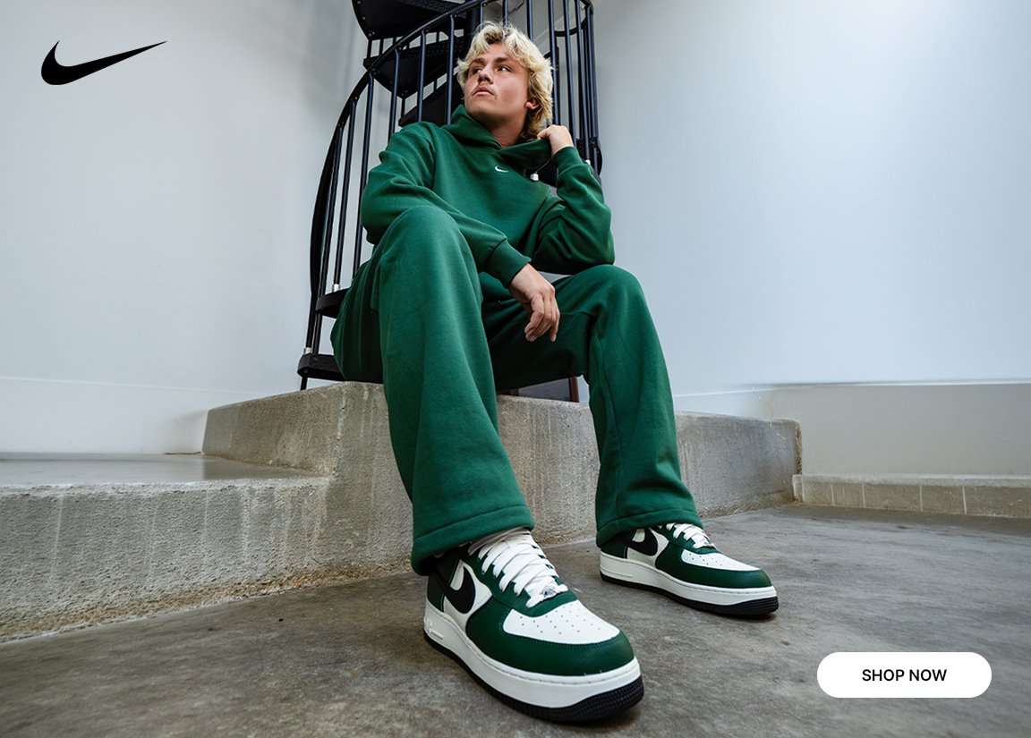 Nike Air Force 1 sneakers in green, white, and black paired with a matching green Nike fleece set in a lifestyle setting.