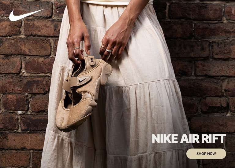 Nike Air Rift sneakers styled with a flowy cream dress against a brick wall backdrop.