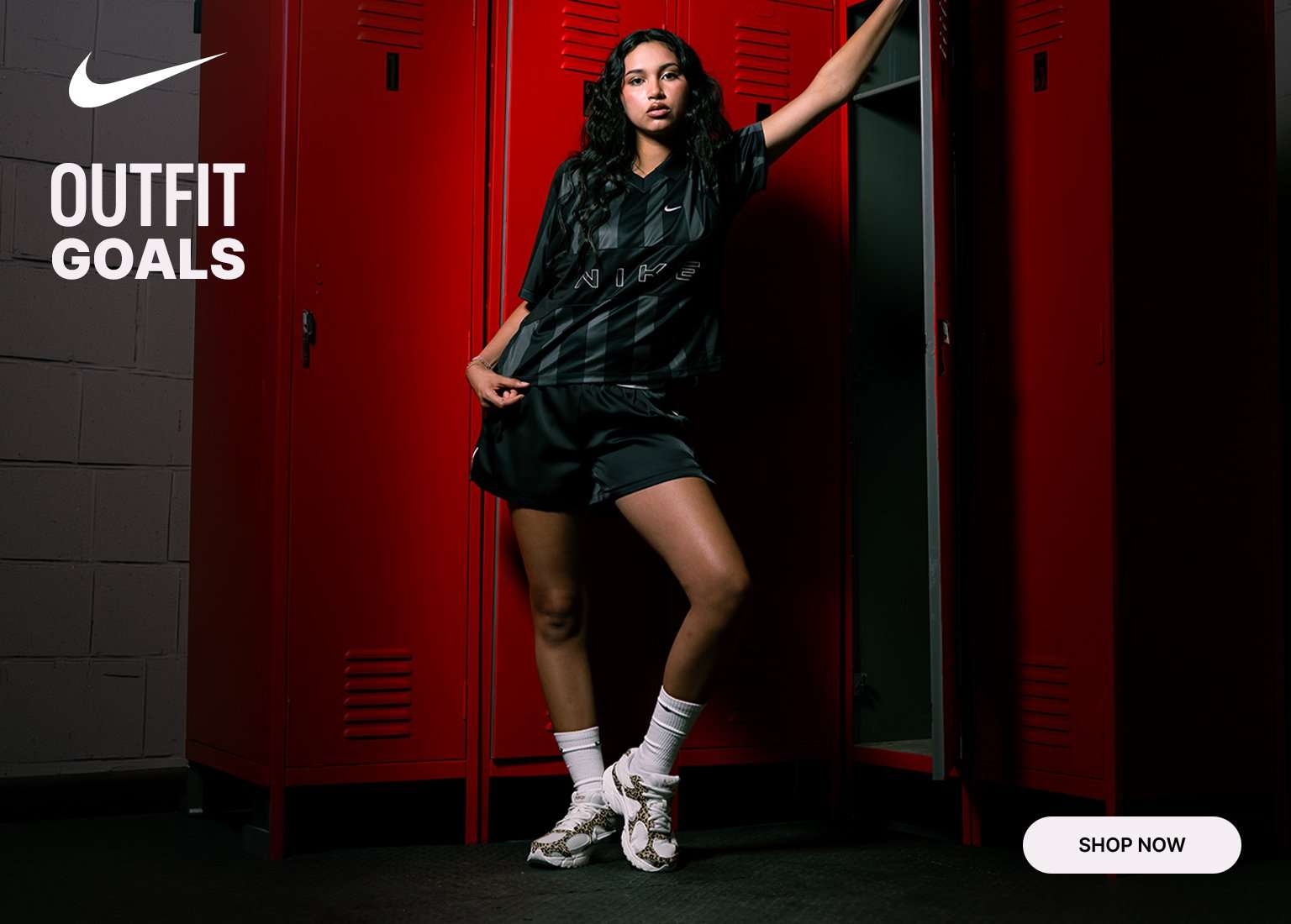 A split-screen Nike advertisement featuring a woman in a black-and-gray striped jersey set against a background of bright red lockers. On the left, a close-up shows her holding a soccer ball, while the right side displays a full-body shot of her posing inside a locker. The center features the Nike swoosh logo alongside the text OUTFIT GOALS, with a SHOP NOW button in the bottom left corner.