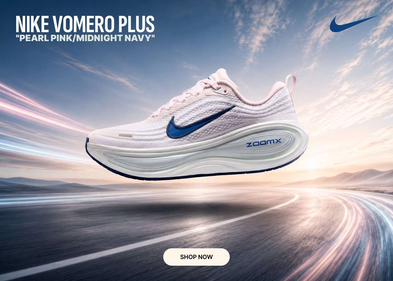 A light pink Nike Vomero Plus running shoe floats above a blurred racetrack under a blue and dawn-lit sky. The shoe features a midnight navy Nike Swoosh and a thick white ZoomX midsole. On the left, white text reads NIKE VOMERO PLUS PEARL PINK/MIDNIGHT NAVY above a cream-colored SHOP NOW button, with a navy Nike logo in the top right corner.