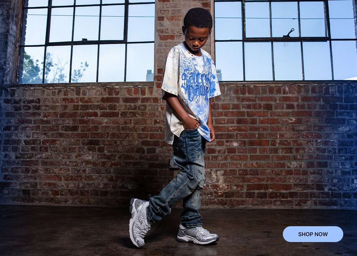 Child modeling oversized graphic T-shirt, distressed jeans and white sneakers in an industrial setting.