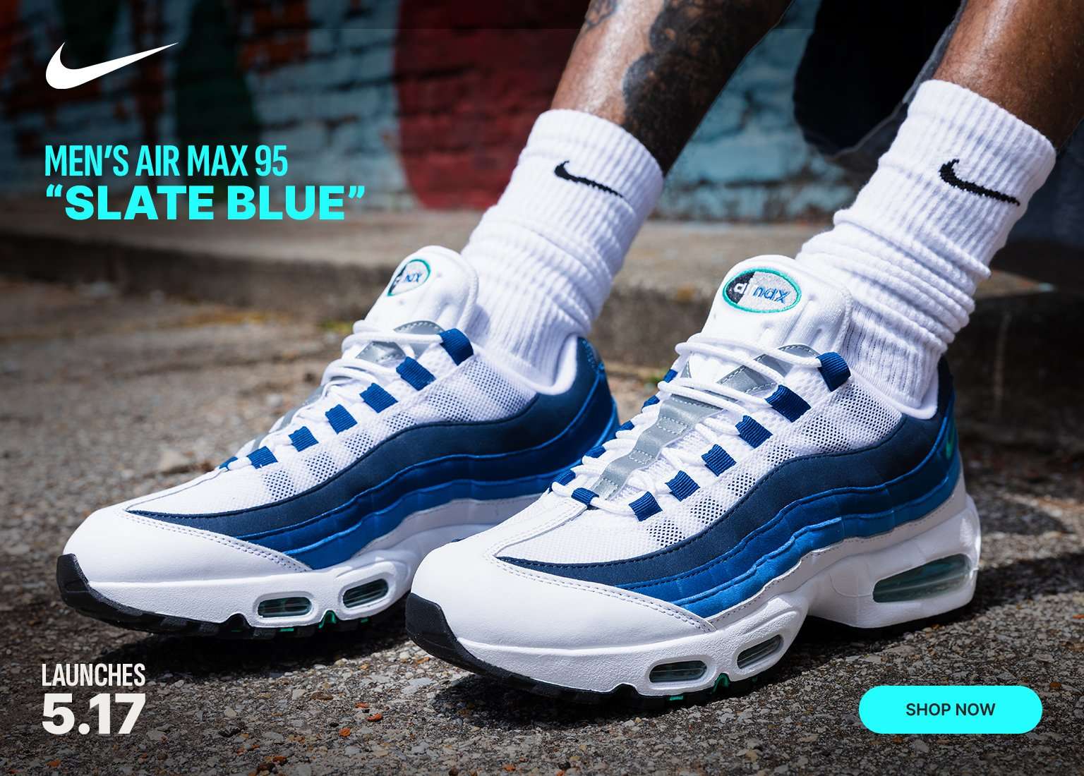 A close-up shot shows a person's feet wearing the Men’s Air Max 95 Slate Blue sneakers in white and shades of blue, paired with white Nike crew socks. The image features a white Nike swoosh and product name in the top left corner, the launch date 5.17 in the bottom left, and a teal SHOP NOW button in the bottom right corner.