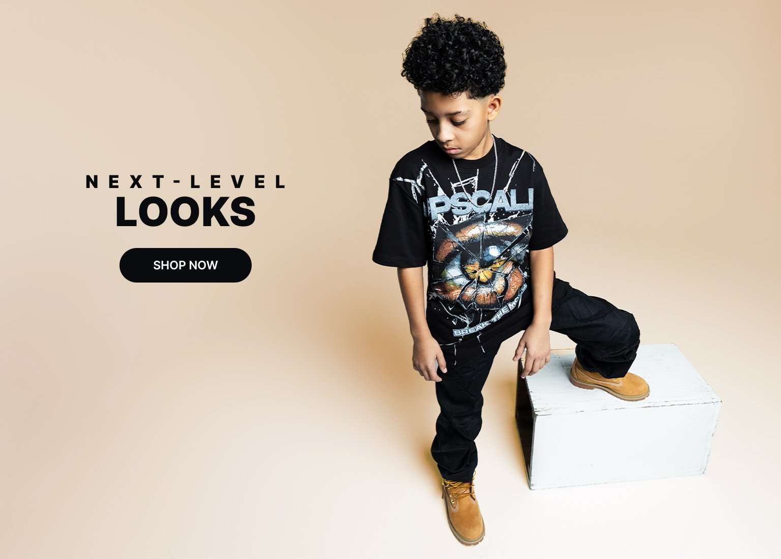 Kids wearing black graphic outfits styled with wheat Timberland boots against a neutral backdrop with Next-Level Looks and Shop Now text.