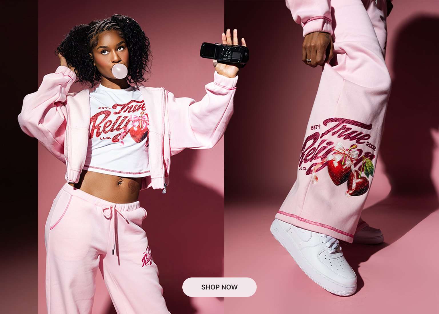 Model wearing a pink True Religion cherry graphic hoodie, tee and sweatpants set with white sneakers against a pink studio backdrop.