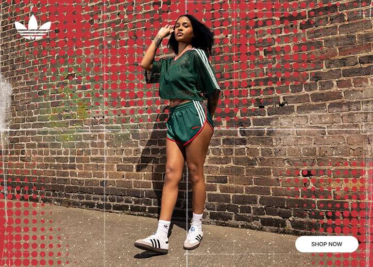 An adidas promotional image featuring a woman posing in a green mesh cropped jersey, matching green shorts with red trim, and white Samba sneakers. She stands against a brick wall overlaid with a red halftone dot pattern and a white grid. An Adidas logo is in the top left, and a Shop Now button is in the bottom right.