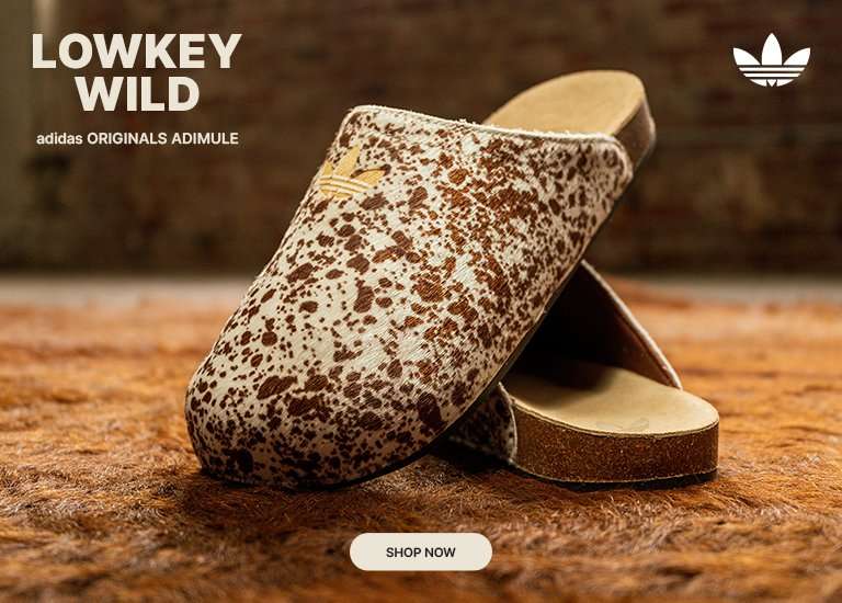 Cowhide-print adidas Adimule clogs displayed on a textured brown surface with matching fur-inspired backdrop.