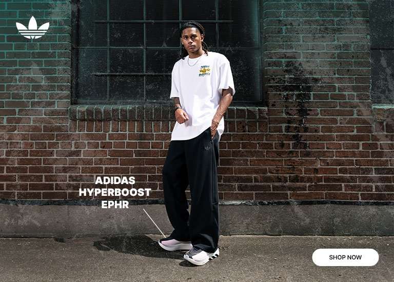 adidas Hyperboost EPHR sneakers in black, white and red with a person wearing a white graphic tee and black pants against an urban brick wall backdrop.