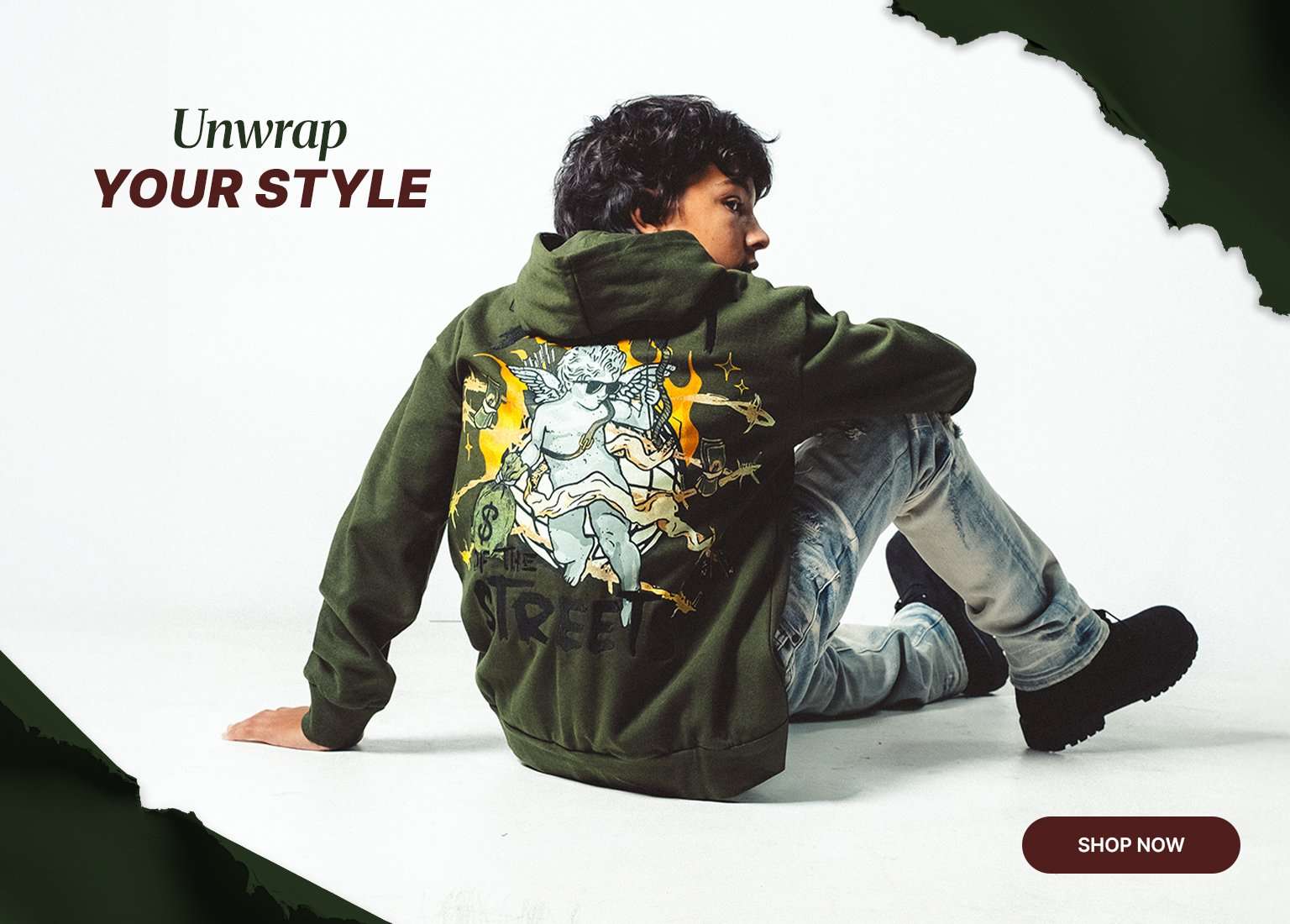 A boy models an olive green graphic hoodie and light-wash distressed jeans. The image shows both the front and back of the hoodie, which features a flame design. Text reads Unwrap YOUR STYLE with a SHOP NOW button.