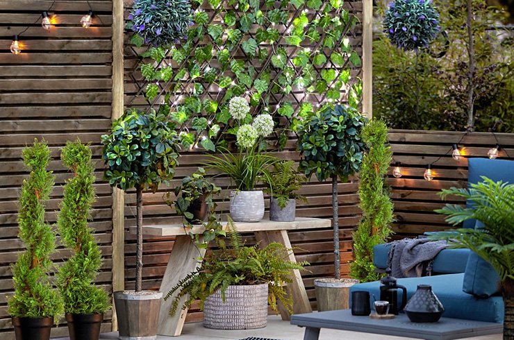 Image of a patio area with plants, outdoor seating and string lights.