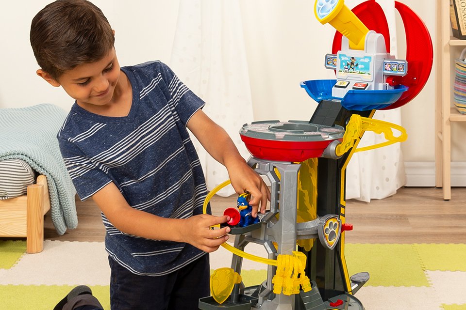 Boy knelt on floor playing with PAW Patrol Mighty Lookout Tower in a living room setting.