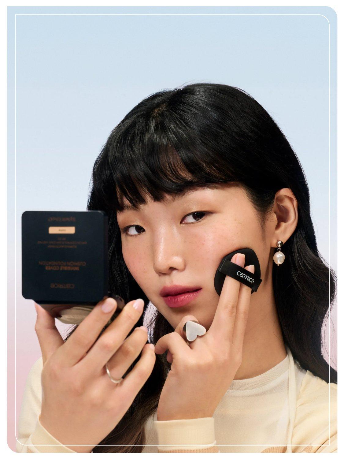 Frau trägt die Catrice Invisible Cover Cushion Foundation mit dem integrierten Applikator auf und hält die geöffnete Cushion Foundation mit Spiegel in der Hand.