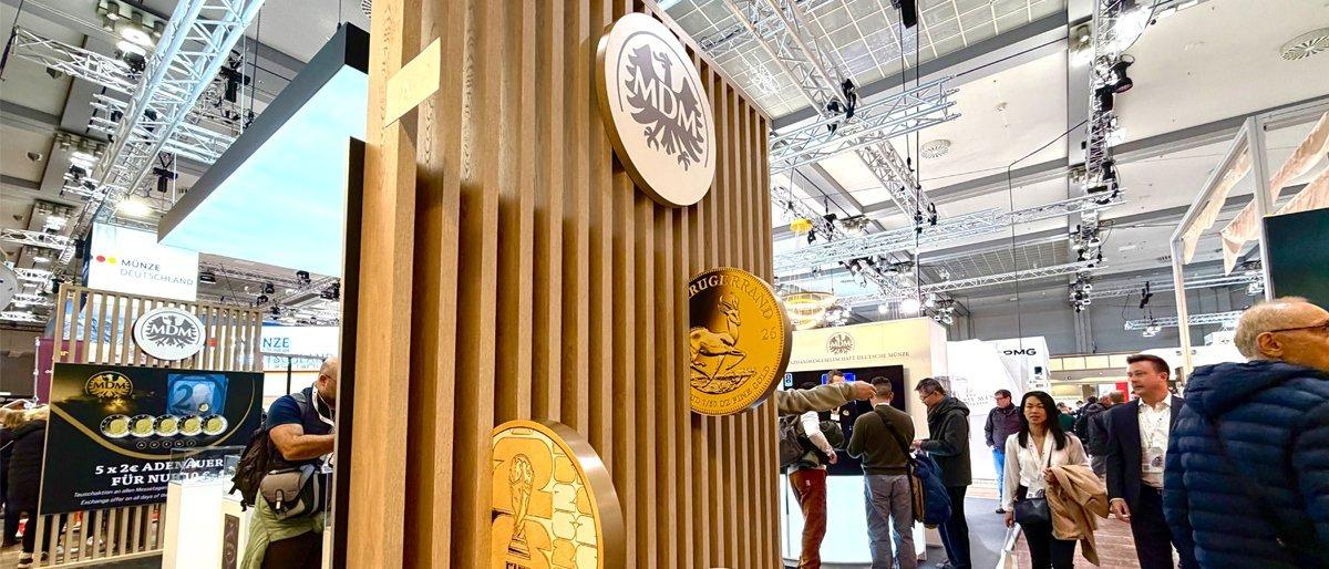 MDM-Messestand auf der World Money Fair mit Goldmünzen-Displays und Besuchern in der Messehalle