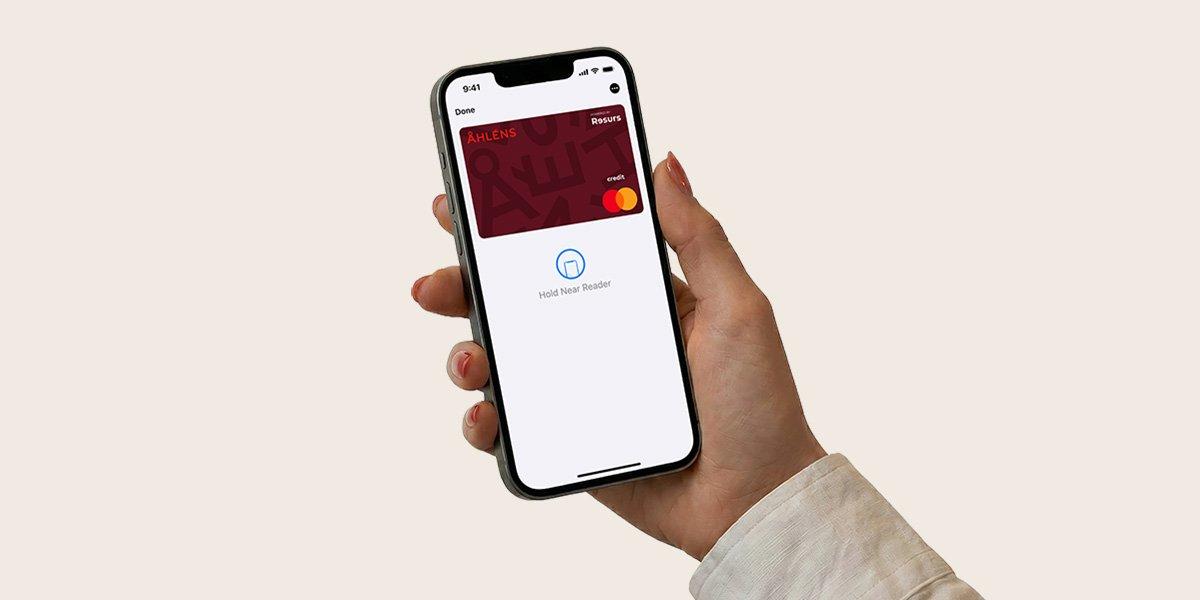 Hand som håller i telefon med ett digitalt Åhléns Mastercard på skärmen.