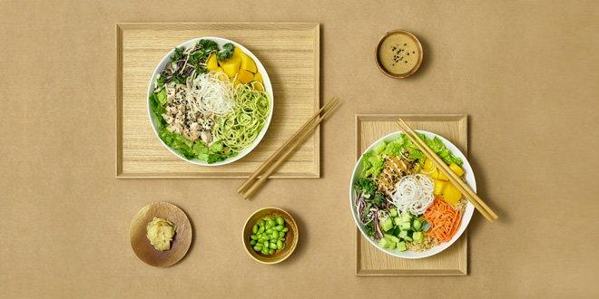 Två poké bowls från Hawaii Poké med färska grönsaker, nudlar och ätpinnar på beige bakgrund.