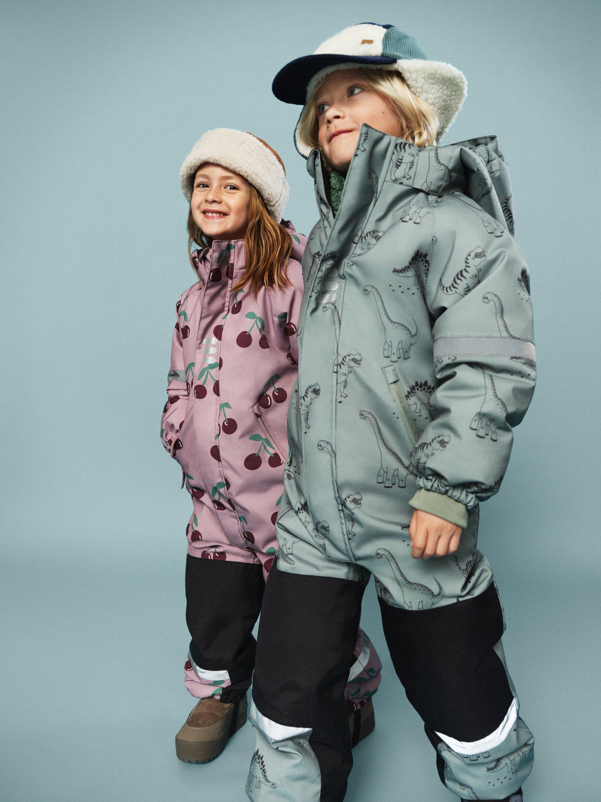 två barn i ytterplagg mot vinröd bakgrund.