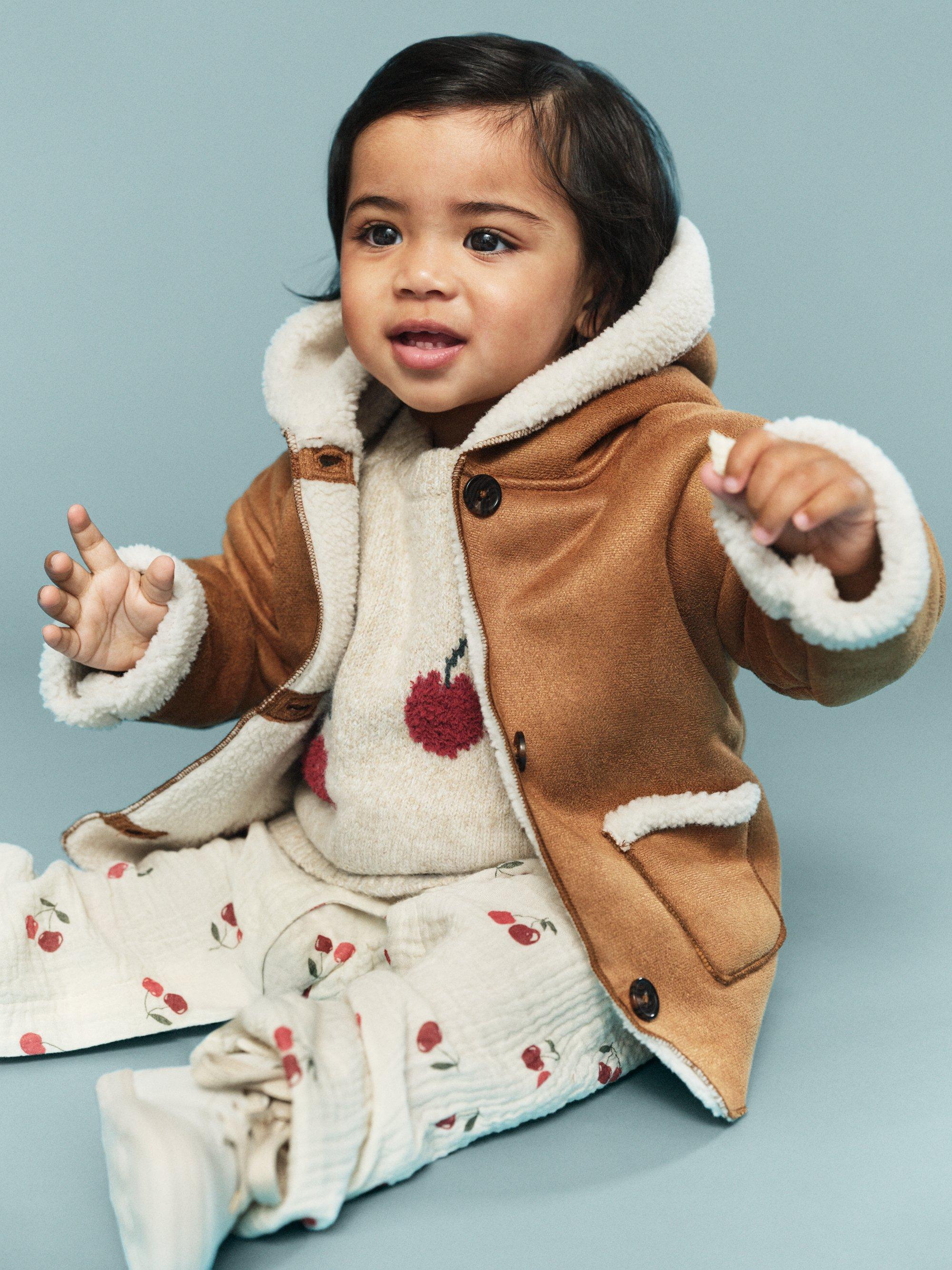 baby som sitter på golvet med en jacka.