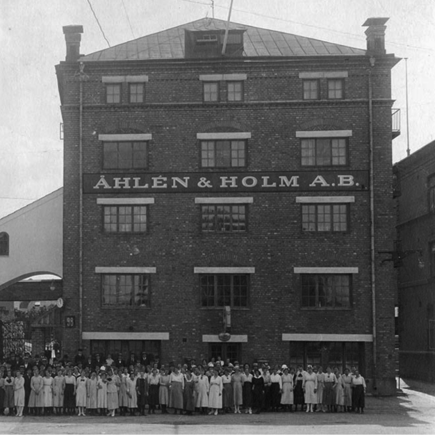 Historisk svartvitt bild på anställda uppradade framför Åhlén & Holms nya lokaler i Stockholm 1915.