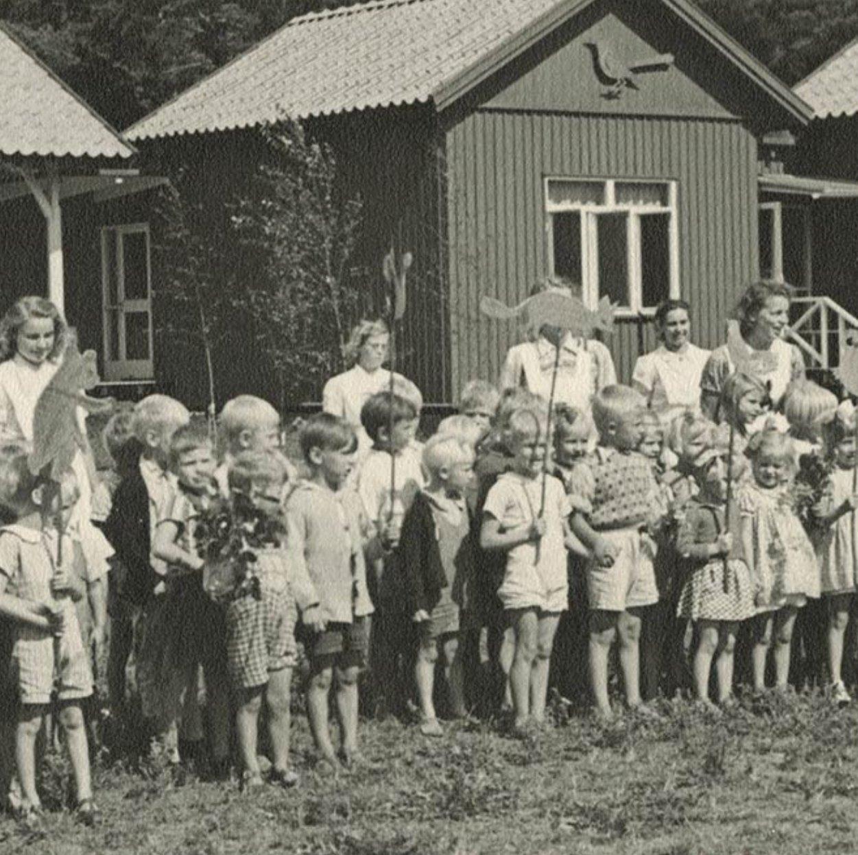 Historisk svartvit bild på barn och fröknar uppradade framför Åhlén & Holms kolonigård på Barnens Ö.