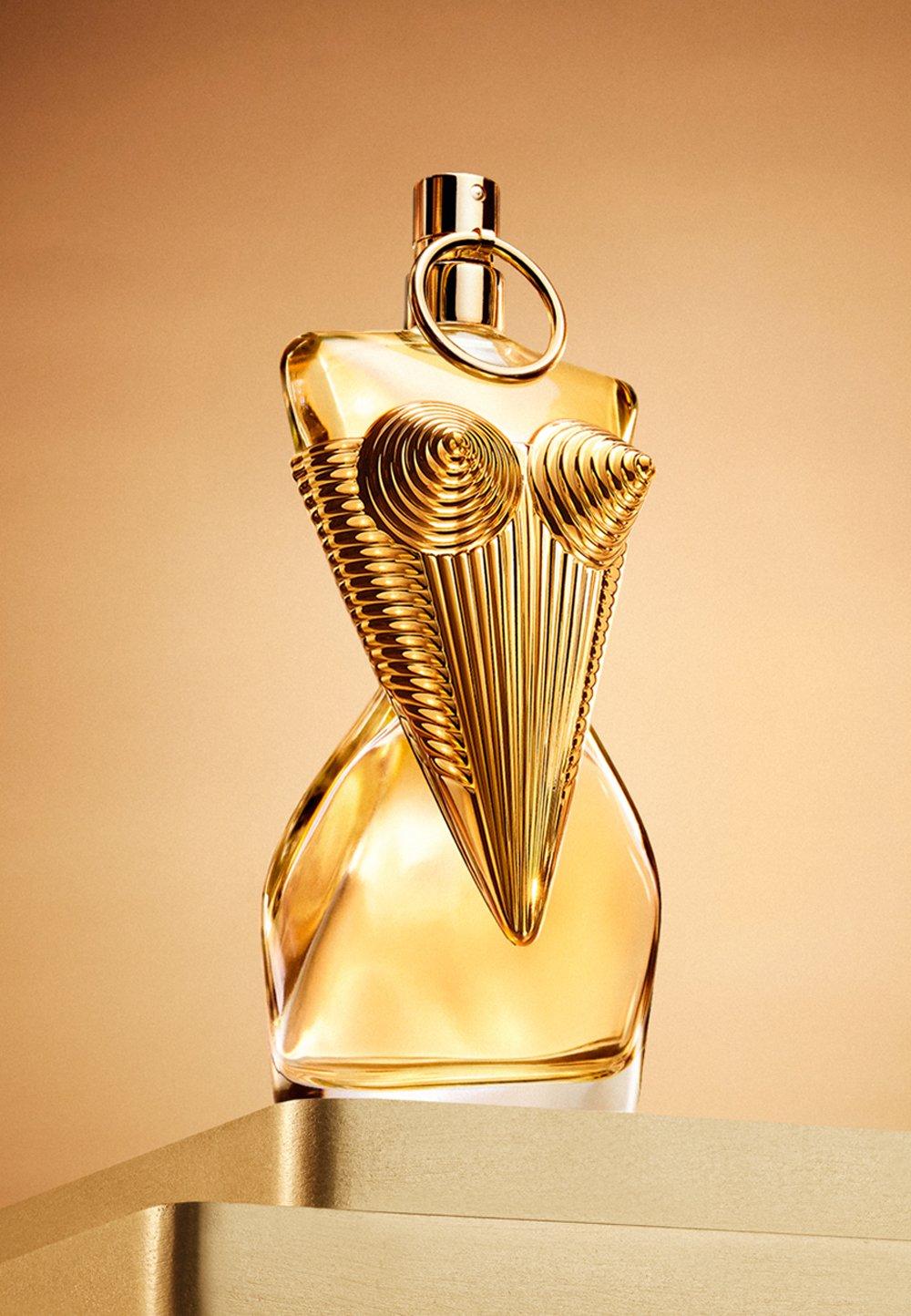 Guldig parfymflaska står på guldig piedestal. 