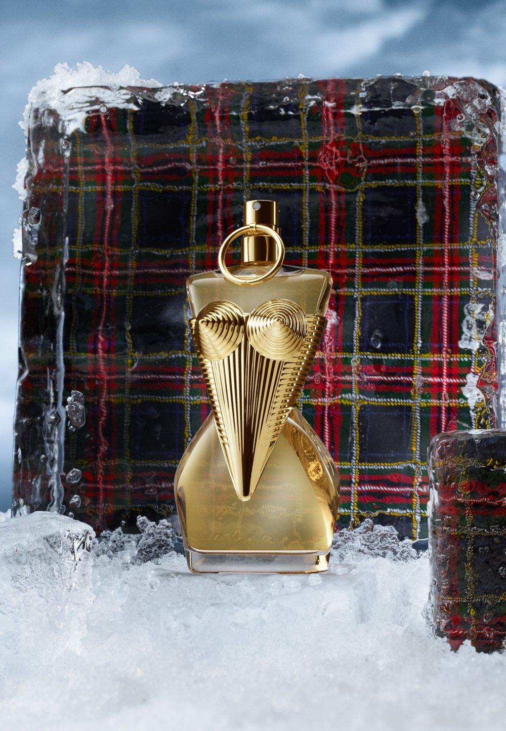 Guldig parfymflaska står på is med en rutig pläd.