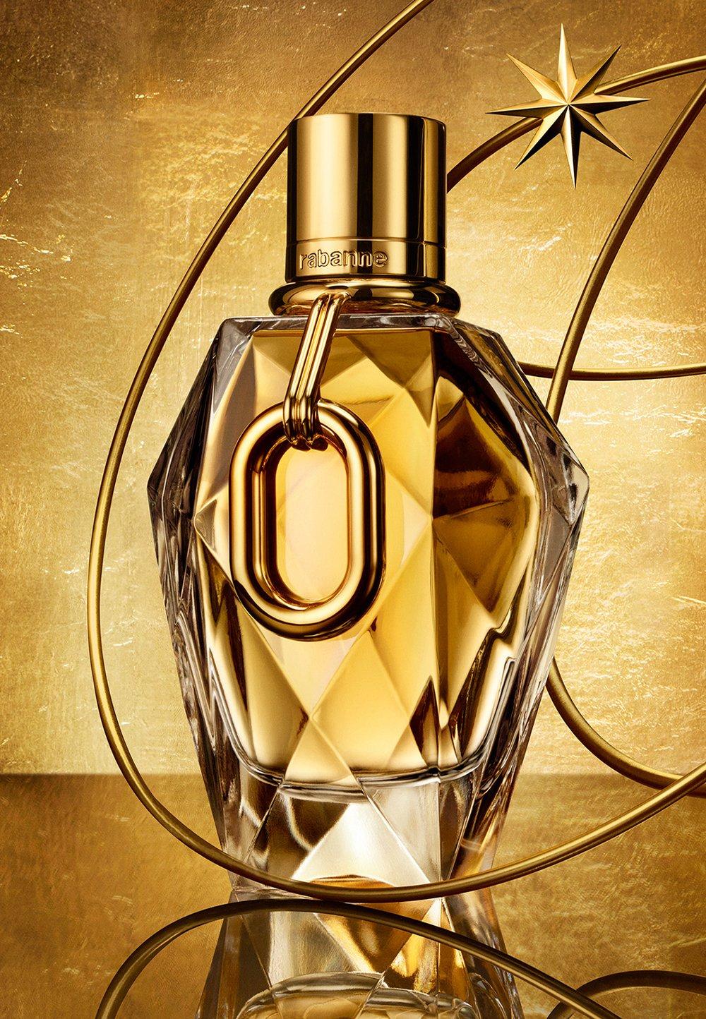 Guldig parfymflaska med avlång berlock står på ett glansigt, guldigt bord.