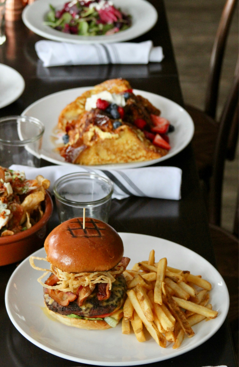Hamburgare med pommes frites och brunchrätt serverade på restaurangbord.