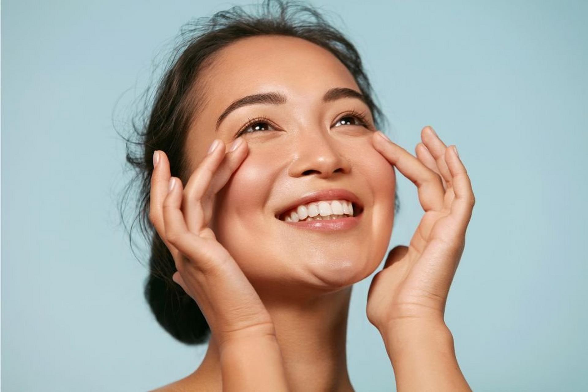 Smiling woman touching her cheeks with both hands.