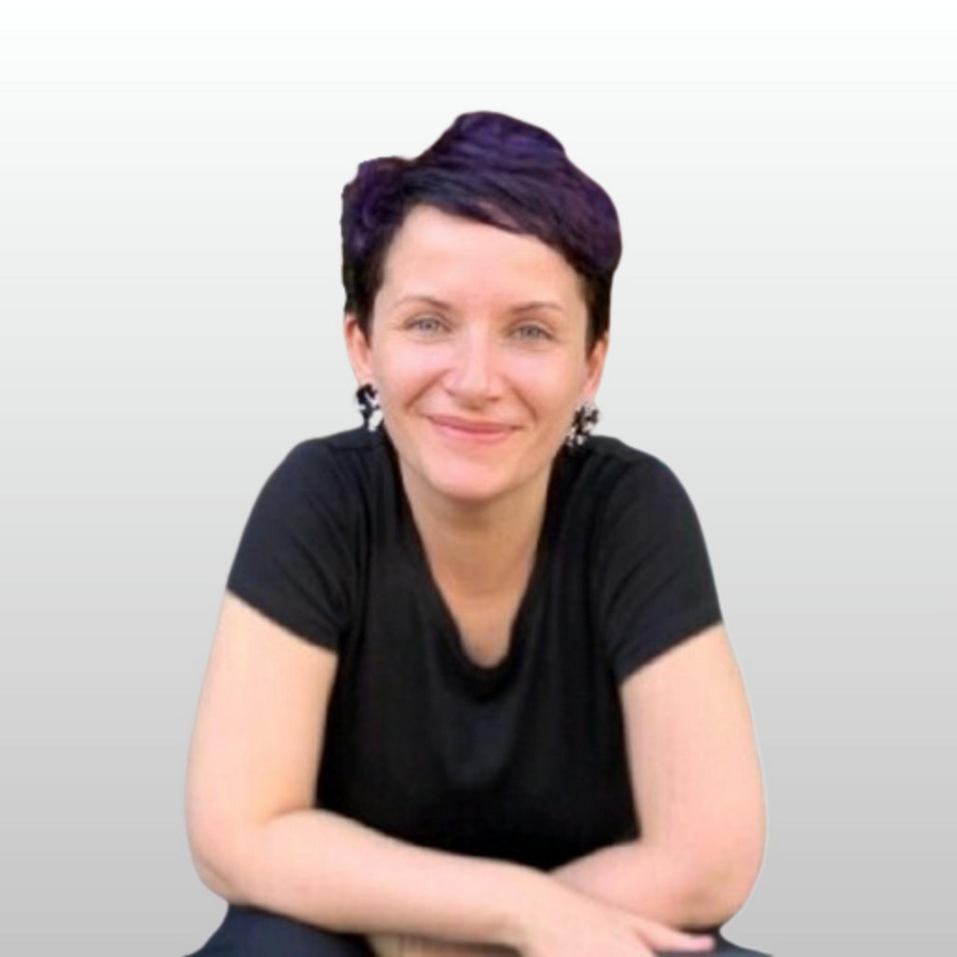 Person with short, dark purple hair wearing a black shirt, sitting with arms crossed.