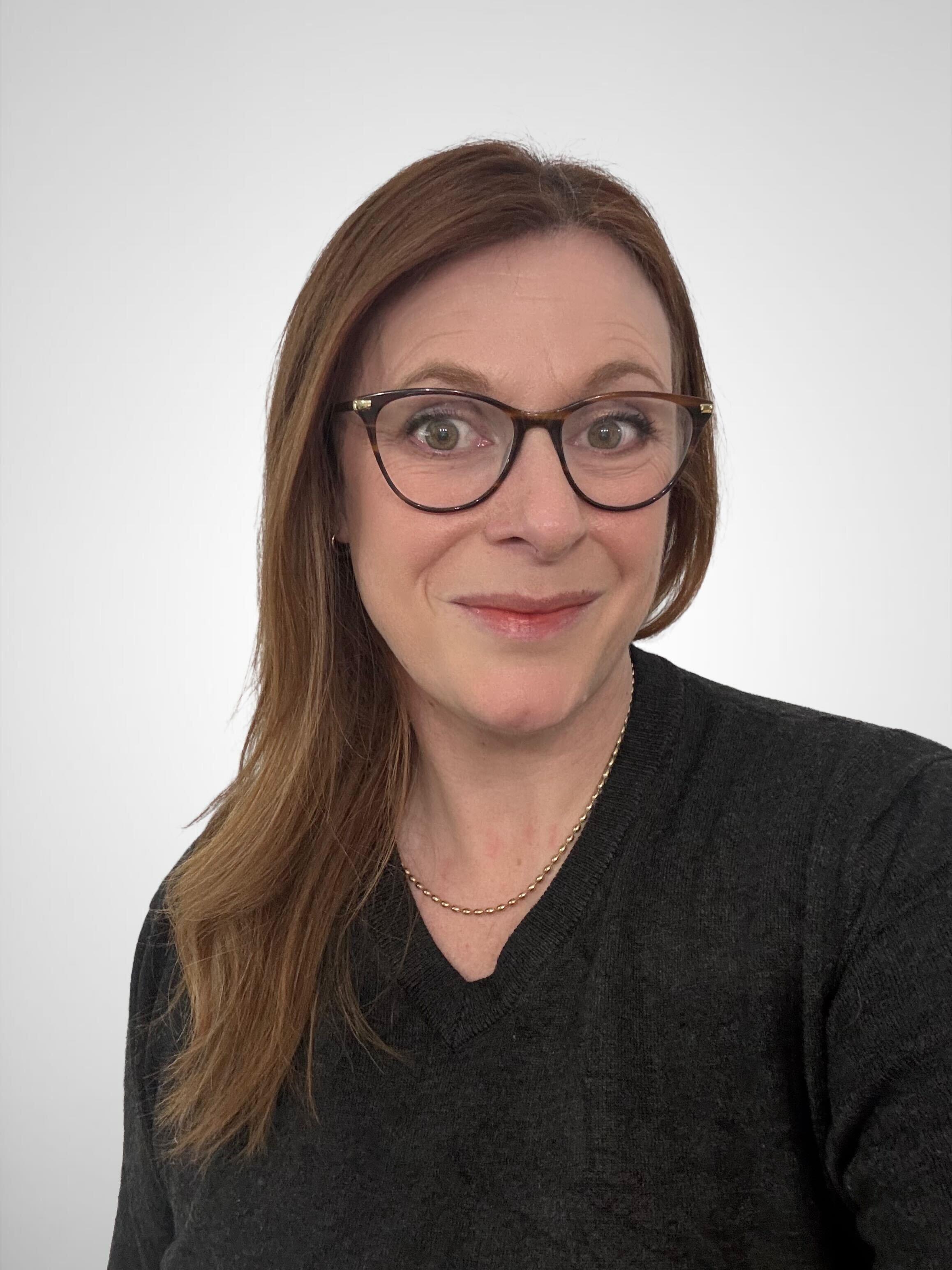 Person wearing a dark sweater and gold chain necklace, with long brown hair.