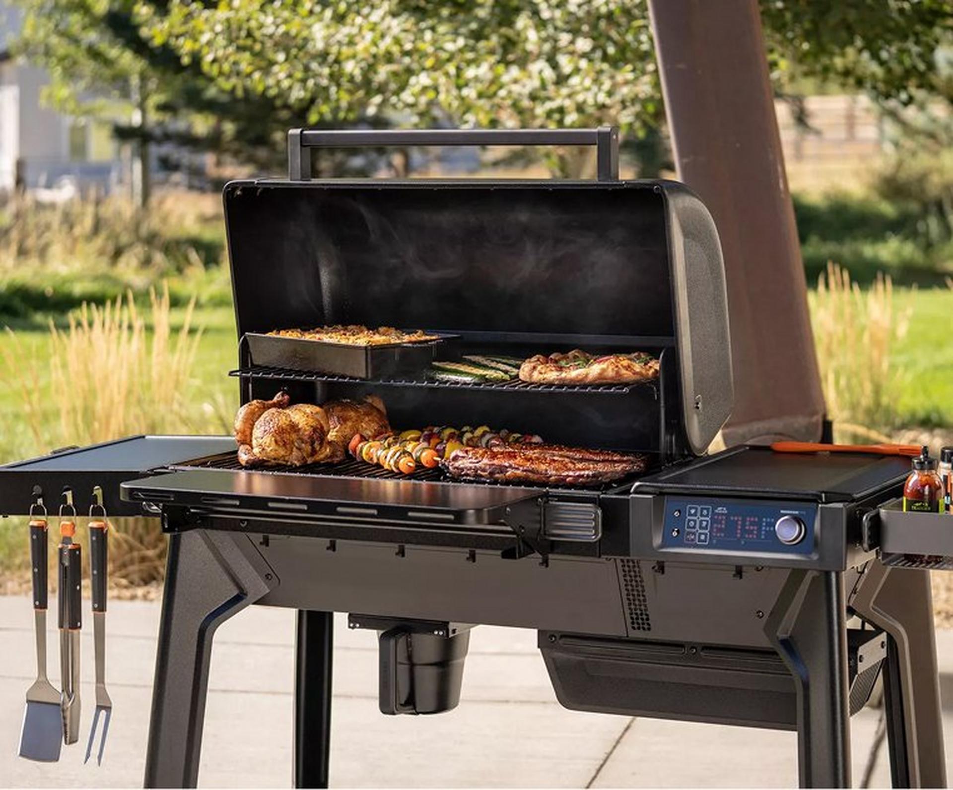 Pellet grill with open lid, cooking ribs, chicken, skewers, and asparagus.