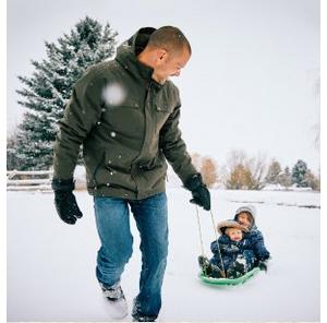 man in green ariat jacket pulling child on sled in snow