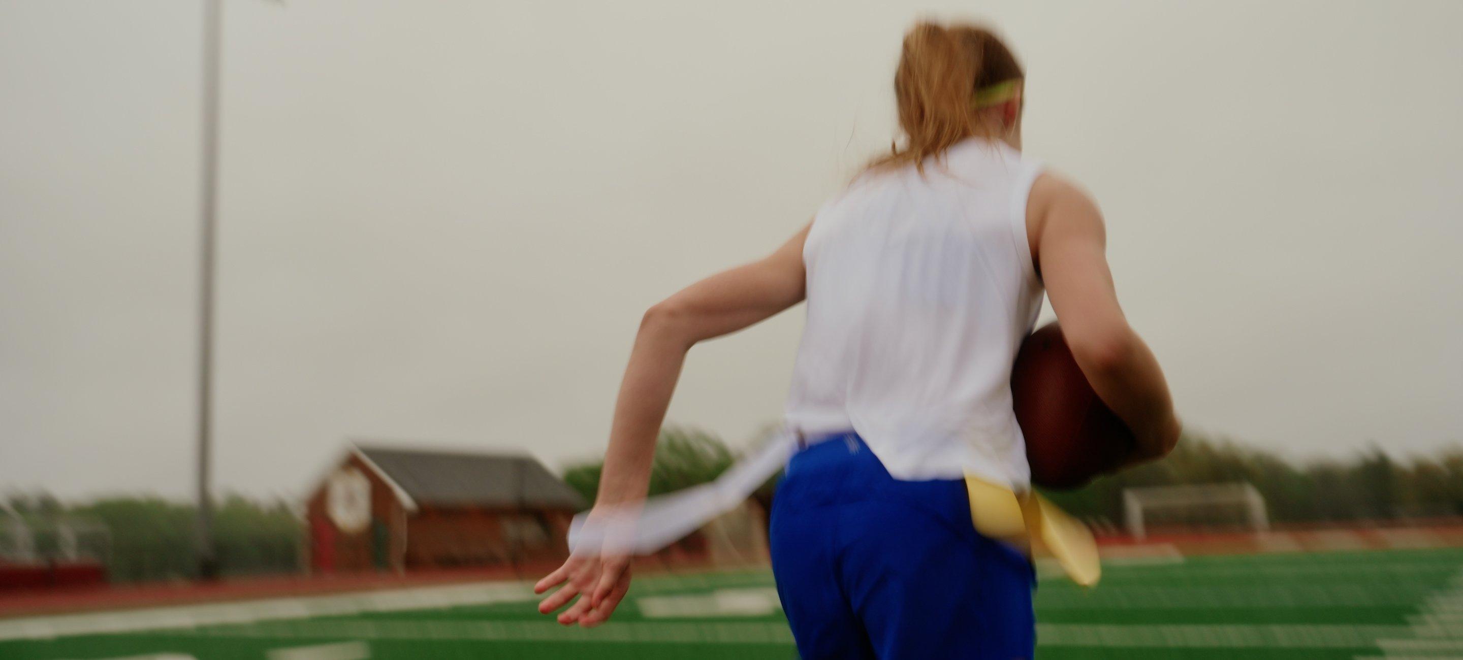 a woman running on a field with a football in her hand