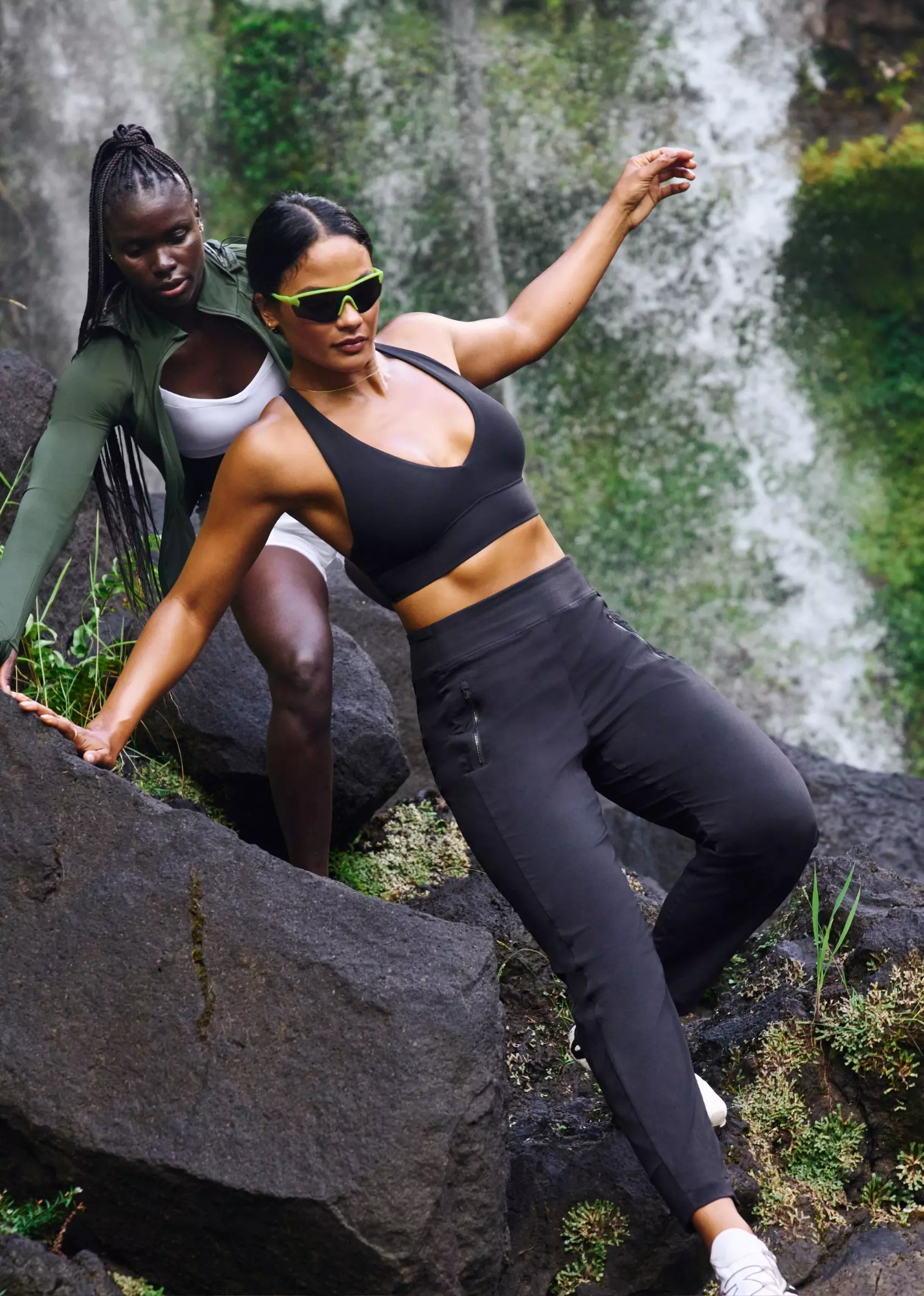 Two women are climbing rocks near a waterfall