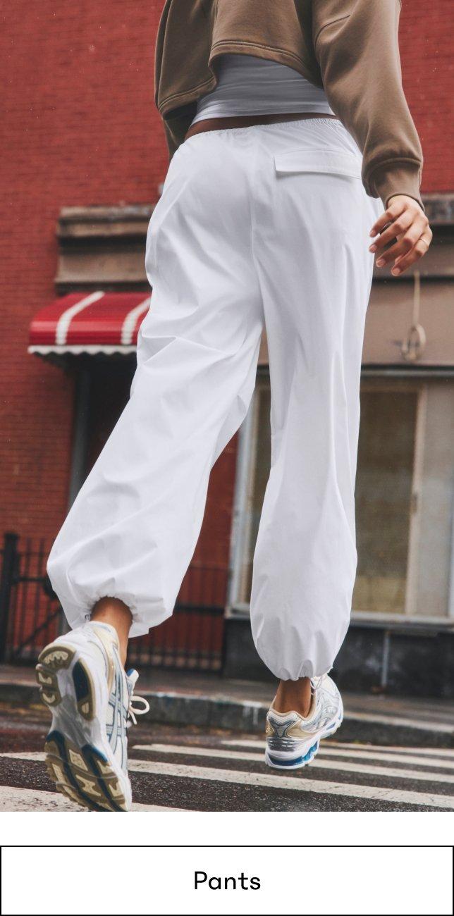 a person walking down the street in white pants and a brown jacket