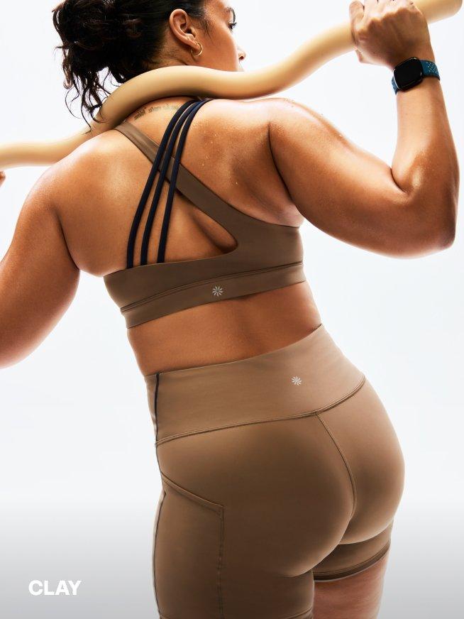 CLAY. a woman in a sports bra and short set holding a large weighted bar during a workout