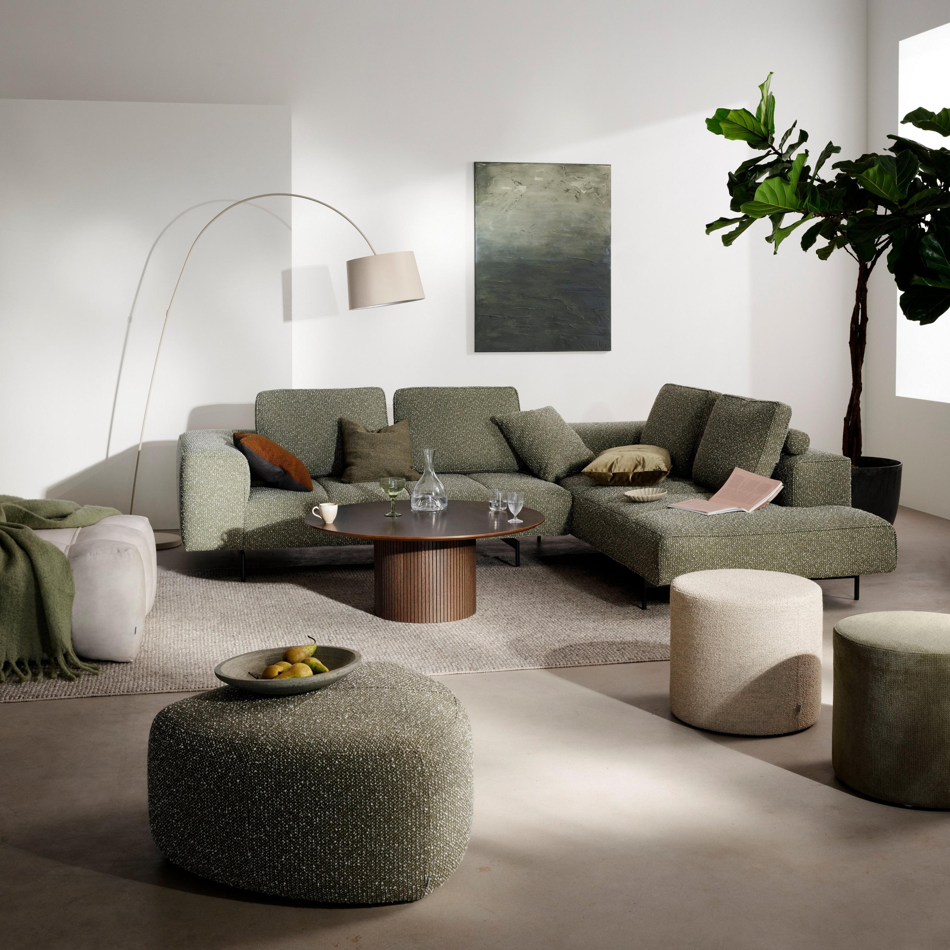 Modern living room with a green sectional Amsterdam sofa, round Santiago coffee table, two Eden footstools, one Nawabari big footstool and one Bermuda footstool, large floor plant, and minimal wall art.